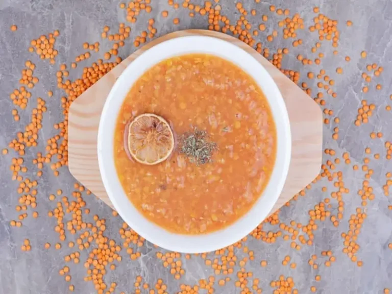 A steaming bowl of lentil soup garnished with fresh herbs, surrounded by vegetables