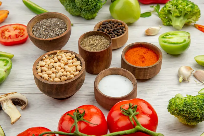 bottom-view-black-eyed-peas-differet-spices-small-bowls-cut-vegetables-grey-table 